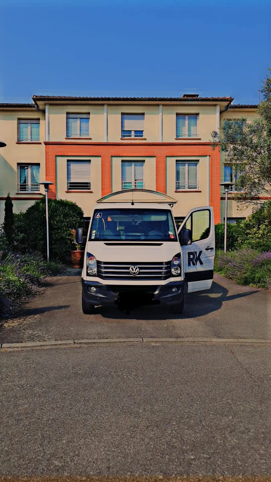 Van TPMR RK-Transports, pictogramme fauteuil roulant sur le pare-brise, devant un établissement